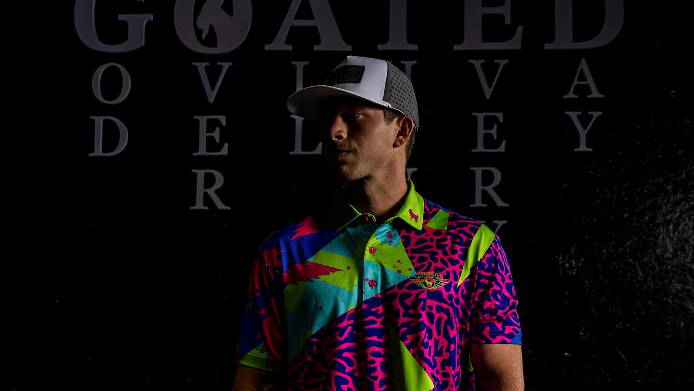 A golfer in a GOATED Golf polo and hat in front of the GOATED wall